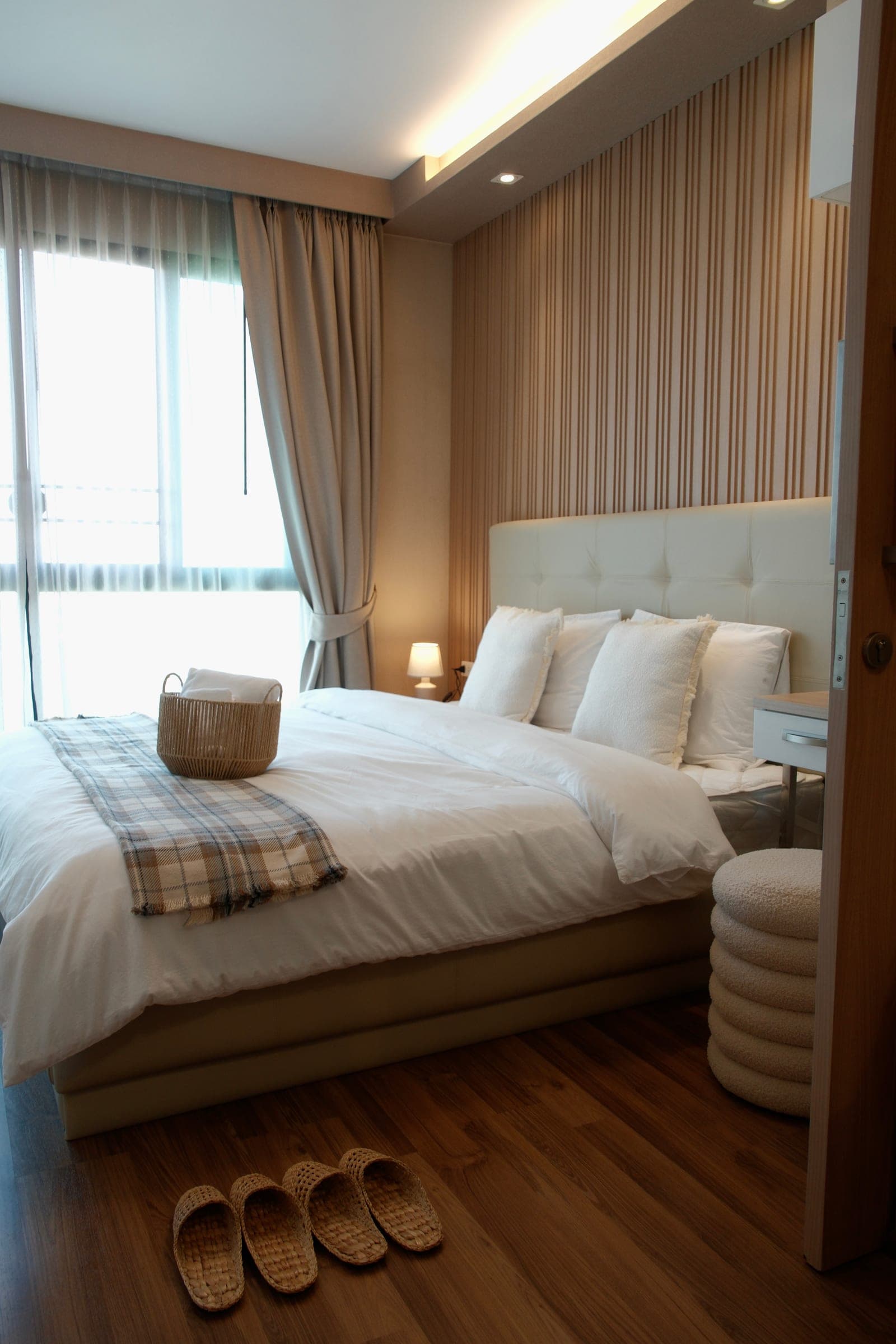 Bedroom with cream tufted headboard, wood-slat wall, white bedding, and warm lighting in a furnished Chiang Mai condo