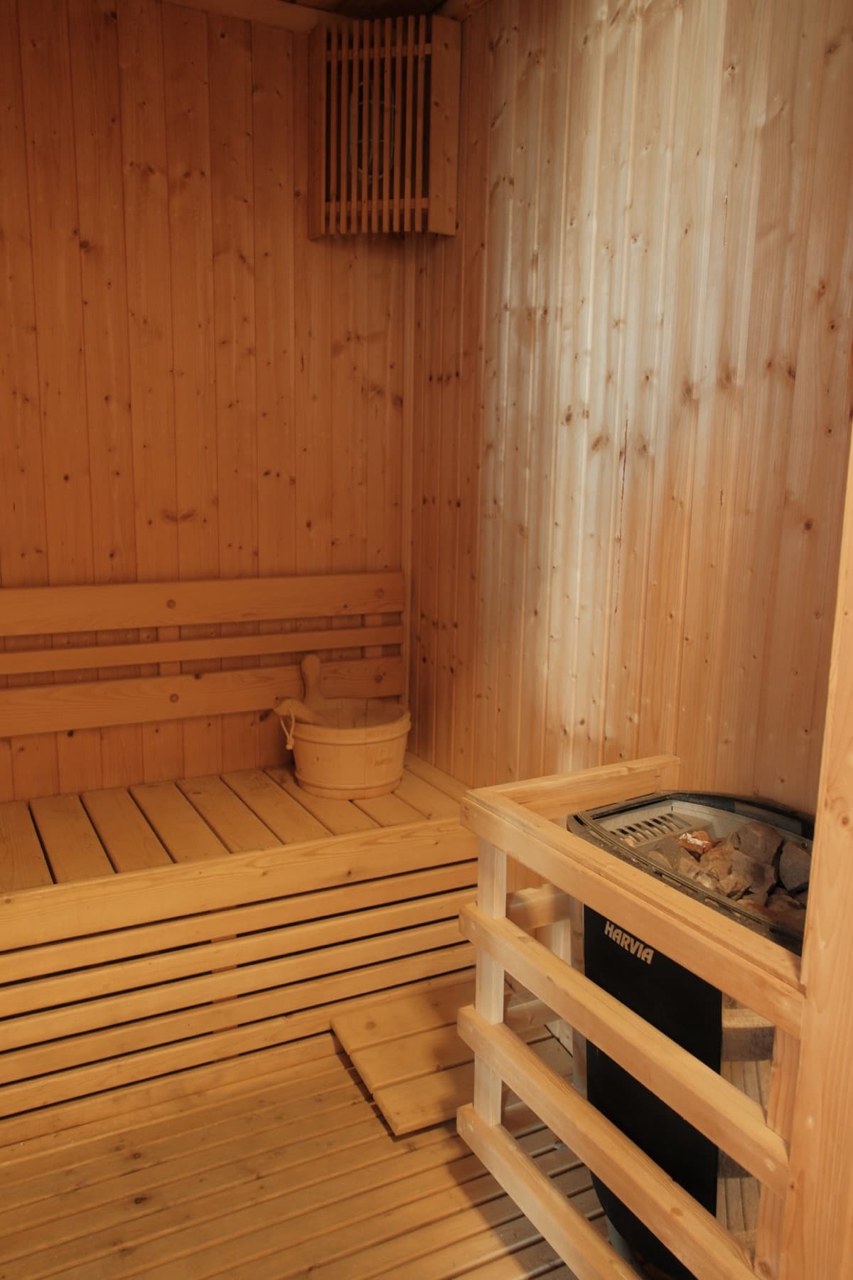 Wooden sauna interior with tiered benches, bucket, and Harvia electric heater